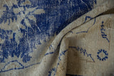 Distressed vintage Oushak rug texture, showing cobalt blue patterns on a soft beige field.
