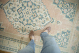 Distressed Oushak rug with pale apricot blush field and dusty navy floral medallion.