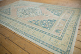 Distressed vintage Oushak carpet corner with abrashed plant borders, pale apricot and dusty navy motifs.
