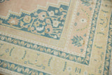 Distressed vintage Oushak rug corner showing pale apricot, dusty navy, and gold floral borders.