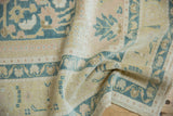 Distressed Oushak carpet pile showing pale gold, dusty navy palmettes, and apricot blush.