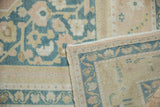 Folded vintage Oushak carpet reveals hand-knotted foundation and distressed pale apricot, dusty navy patterns.