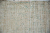 Distressed Oushak rug with worn pile, visible foundation, in faded ivory and seafoam green.