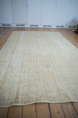 Distressed vintage Oushak carpet displaying worn texture with ivory, cream, and seafoam green hues.