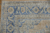 Corner detail of a distressed Oushak carpet highlighting its worn pile and cobalt blue floral border.