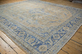 Angled view of the vintage Oushak's corner showing textured wear on the cobalt blue Rococo-style border.