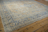 Angled view of the worn texture and cobalt blue floral border on a distressed Oushak rug.