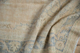 Distressed Oushak carpet border with faded denim blue arabesque motif, worn texture, and fringe.
