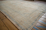 Distressed texture of a vintage Oushak rug with sand field and faded blue border.