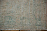 Close-up of distressed vintage Oushak rug corner, showing worn pile, subtle green lines, and fringe.