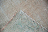 Distressed Oushak carpet corner showing wear to knot heads, visible foundation, and selvage.