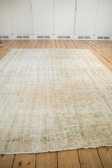 Distressed texture with cream and pale sage tones, showing exposed foundation at the rug edge.