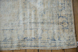 Distressed vintage Oushak rug showing worn cream pile, faded blue pattern, and fringe.