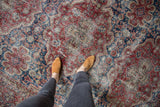 Distressed vintage Oushak carpet displaying textured midnight blue and black cherry floral motifs.