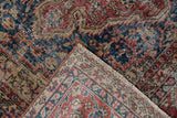 Folded corner of vintage Oushak showing distressed dark pile, geometric light foundation, and fringe.