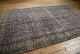 Distressed Oushak rug showing antique ivory border and aubergine field with vine motif.