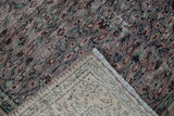 Distressed Oushak rug corner revealing worn aubergine pile, intricate weave, and fringe.