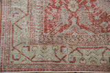 Vintage Sivas carpet corner showcasing distressed geometric vine border in brick red and silver.