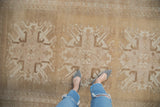 Distressed Oushak carpet with starburst floral design and vinery on an abrashed beige field.