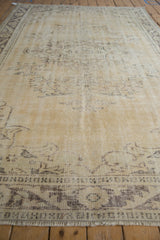 Distressed beige Oushak rug's worn pile texture and faded charcoal meandering vine border.