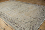 Distressed corner of a vintage Oushak carpet, showing faded floral vine border and fringe.