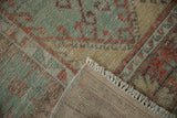 Folded corner of a distressed Oushak rug showing the woven back, hand-knotted pile, and fringe.