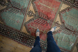 A close view of the distressed texture and finned motifs in mint green and red on a vintage Oushak runner.