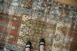 Close-up on the distressed Oushak runner showing sage green and rust geometric designs worn to the pile.