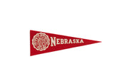 Vintage red felt Nebraska University pennant, featuring white school crest and text, 3.5x9.5 inches.