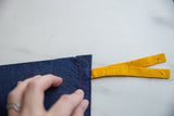 Vintage blue felt pennant corner, showing red stitching, yellow felt ties, and pinholes.