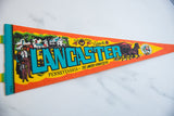 Close-up of vintage felt pennant showing teal LANCASTER text and Amish homestead details.