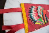 Red vintage felt pennant showing visible pinholes, wear, and colorful chief graphic.