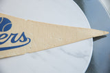 Vintage felt pennant showing blue 'ers' lettering, worn beige texture, and pointed tip.