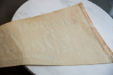 Reverse of vintage felt pennant, showing beige texture, creases, pinholes, and faint red staining.