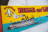 Yellow felt pennant with red 'BELLE OF LO' text, white fleur-de-lis, and steamboat design.