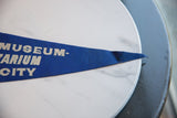 Vintage blue felt pennant's pointed tip with 'MUSEUM-' text, showing light creasing.
