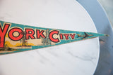 Felt pennant featuring red 'CITY' text, Rockefeller Center, and vintage airplane.