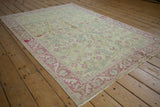 Distressed Sparta rug from an angle, with a lime green field and dusty blush floral border.