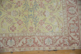 Corner detail of the vintage rug's meandering floral border in dusty pink, blue, and beige.