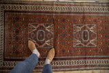 Rust-aubergine Afghani Belouch rug detail: squared medallion, vinery, and visible knot heads.