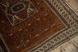 Vintage Afghani Belouch rug with textured rust field, aubergine vinery, and patterned border.