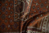 Folded vintage Afghani Belouch rug showcasing textured pile and stepped geometric patterns in rust, aubergine, and ivory.