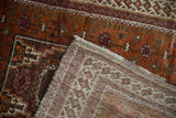 Vintage Afghani Belouch rug's rust pile with aubergine gul, hand-knotted backing, and fringe.