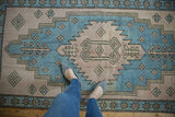 Feet on vintage distressed Oushak rug, showing faded sky blue and dusty mauve patterns.