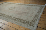 A vintage Oushak's spacious, faded field and detailed geometric border seen at an angle.