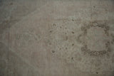 Exposed black wefting showing through the short, pale dusty rose pile of the distressed carpet.