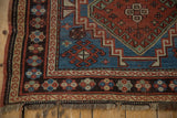Vintage Caucasian rug corner with geometric guls, madder red border, and worn fringe.