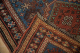 Vintage Caucasian rug detail showing geometric guls, madder red, indigo blue, and fringed corner.