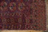 Vintage Turkmen rug corner with geometric guls, chestnut and fuchsia borders, and tattered fringe.