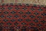Close-up of vintage Turkmen rug, geometric floral guls in chestnut, fuchsia, navy, with worn fringe.